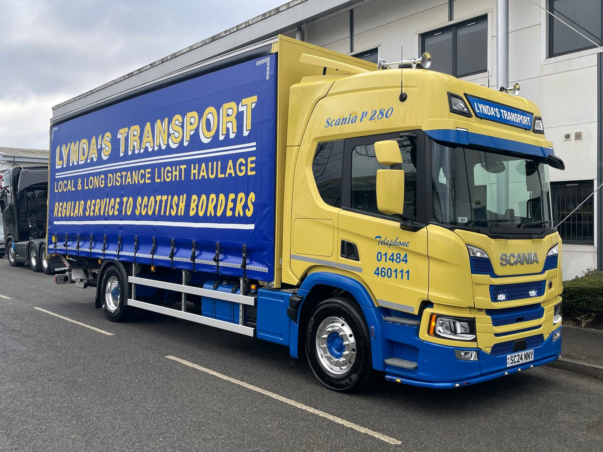 Lynda's Transport yellow curtainside truck outside an industrial building