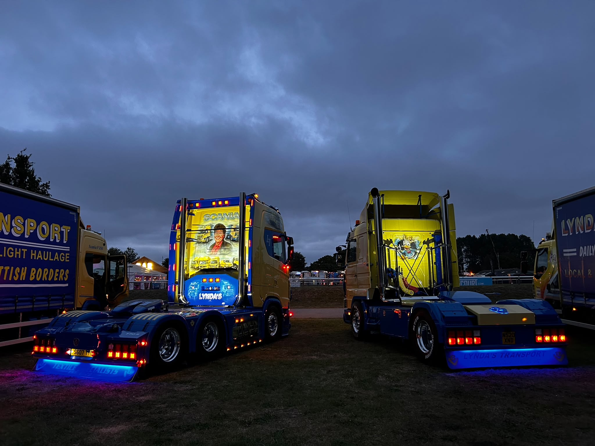 Two illuminated Lynda's Transport tractor units parked at dusk