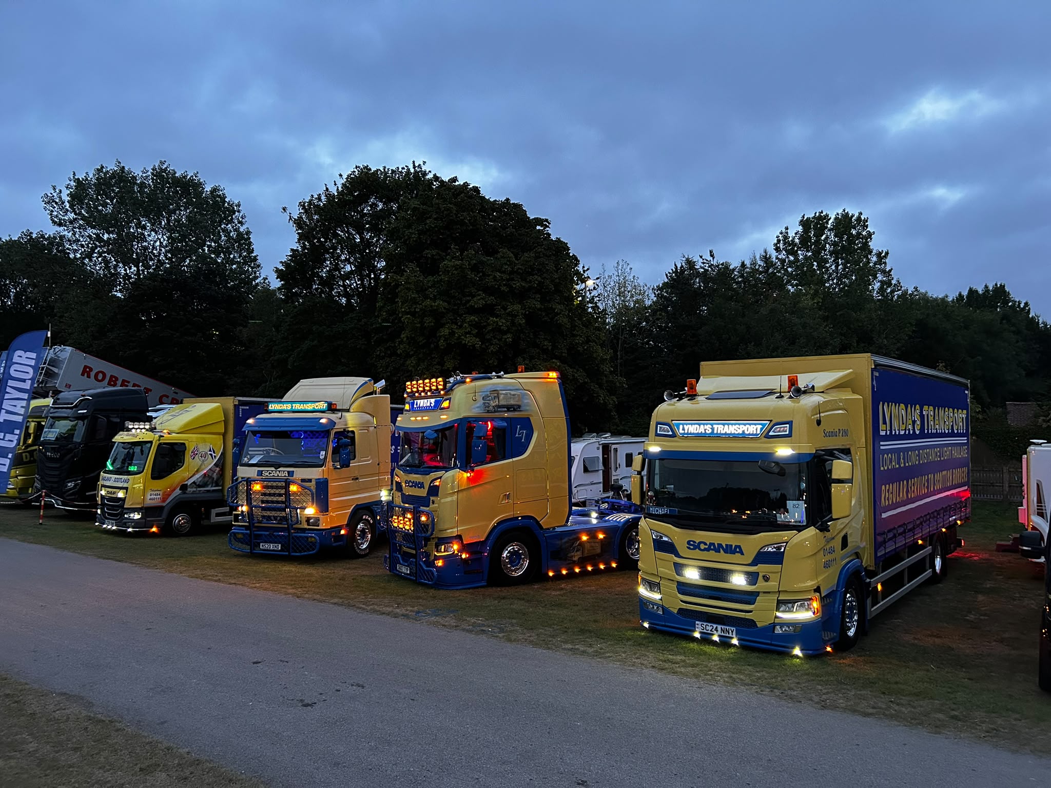 Lynda's Transport fleet line-up with headlights on in the evening